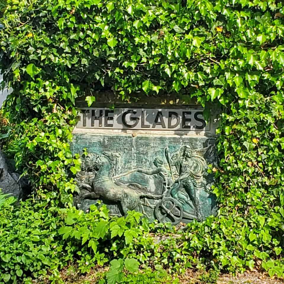 At the entrance of The Glades Woodland Garden Surrey British Columbia Canada, there is a gated drive. Rhododendrons are visible from the roadside.