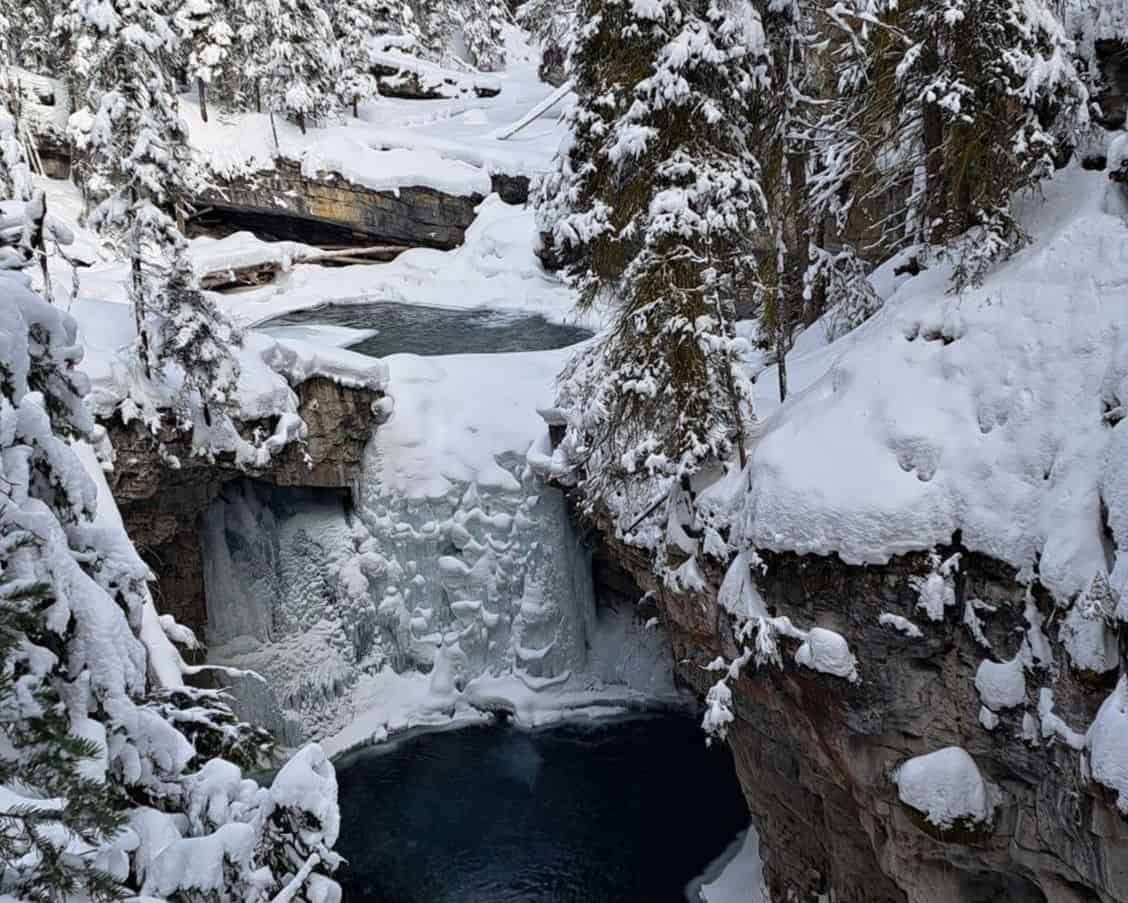 A beautiful winter scene in Johnston Canyon in Banff. A forzen waterfall connects to deep blue pools of still flowing water.