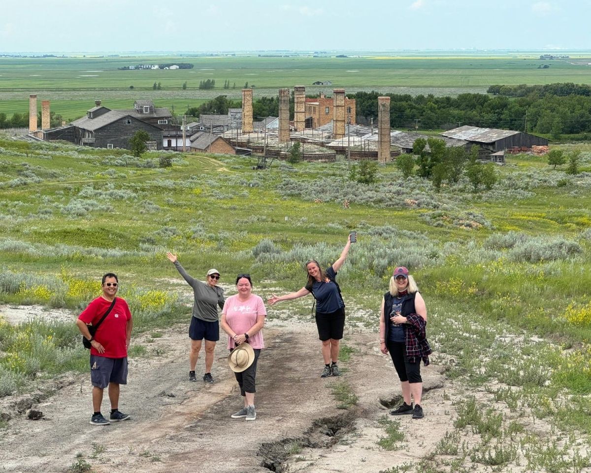 A group of 5 Canada Adventure Seekers pose for a picture with the Claybank Brick Plant in the background.