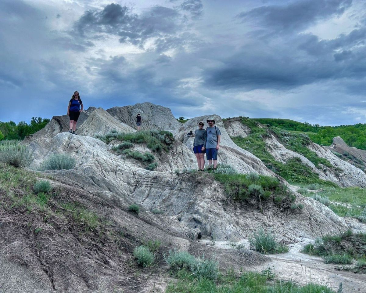 With a cloudy sky in the background, three adventure seekers stand atop the clay pits at  various heights at the Claybank National Historis Site in Saskatchewan.