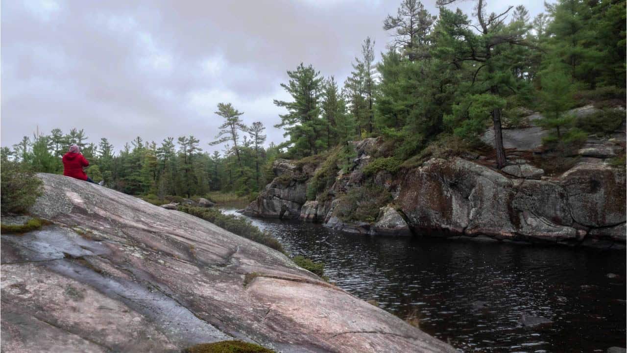 Sitting by the river on the rocks of the Canadian Shield on the Gut Lake Trail in Ontario Canada.