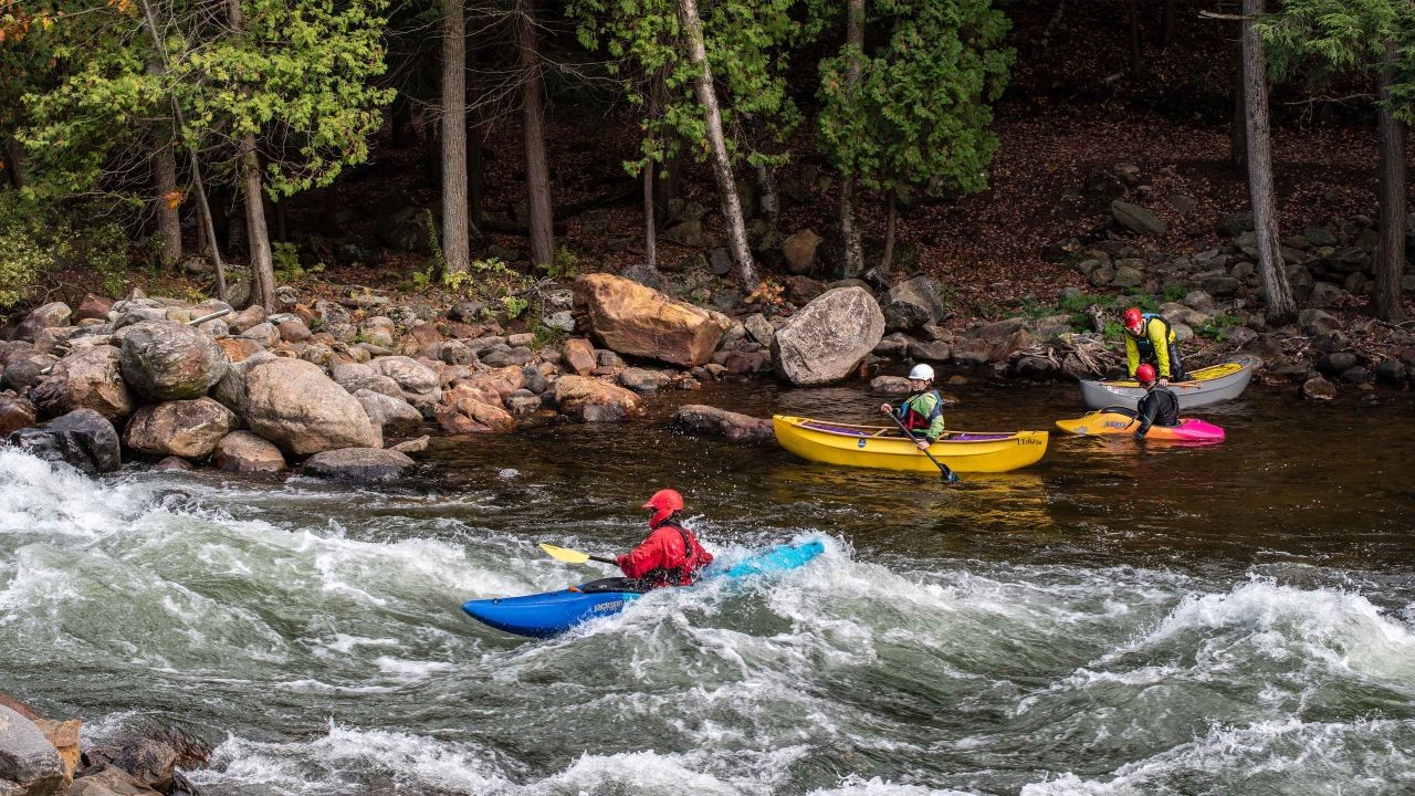 Three kayakers watch as others navigate the rapids on the Gull River in the reserve.