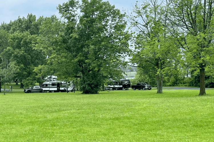 A green grass field, with two campers and two trucks behind lush trees in Ontario, Canada